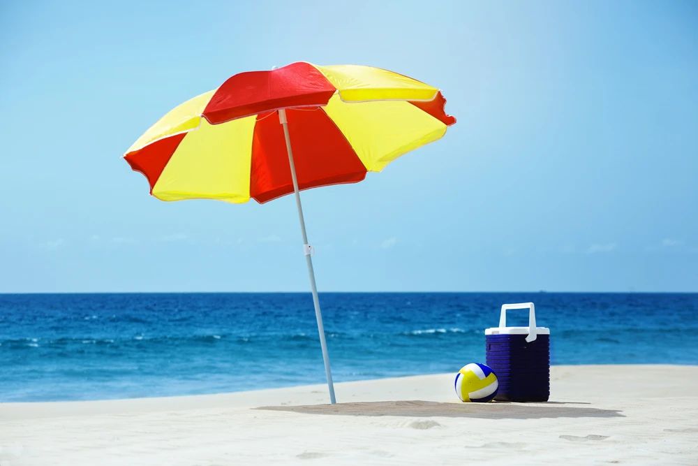beach umbrella, cooler, and ball in the sand